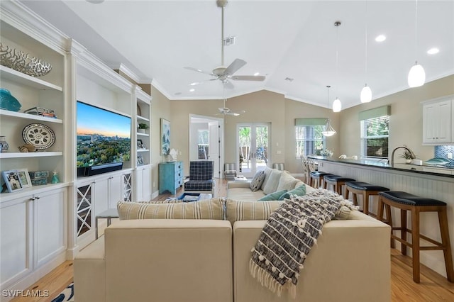 living room featuring built in shelves, visible vents, light wood-style floors, vaulted ceiling, and crown molding