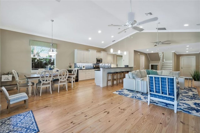 living room with visible vents, stairway, light wood-style flooring, and crown molding