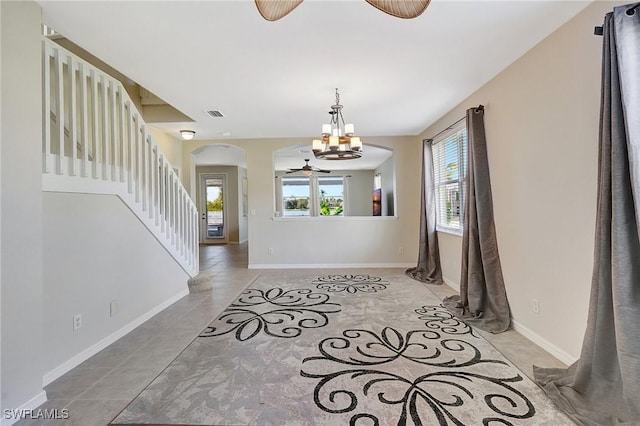 foyer featuring arched walkways, baseboards, visible vents, ceiling fan with notable chandelier, and stairs
