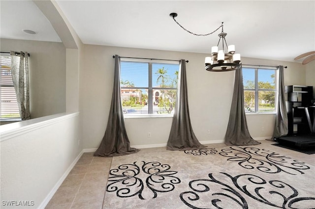unfurnished dining area featuring a chandelier, plenty of natural light, arched walkways, and baseboards