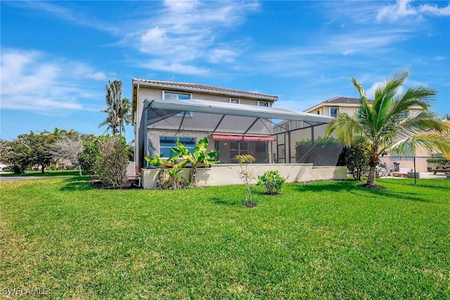 rear view of house with fence, a lawn, a lanai, and stucco siding