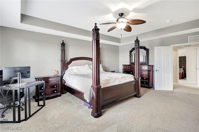 bedroom featuring a tray ceiling, ceiling fan, visible vents, and light carpet