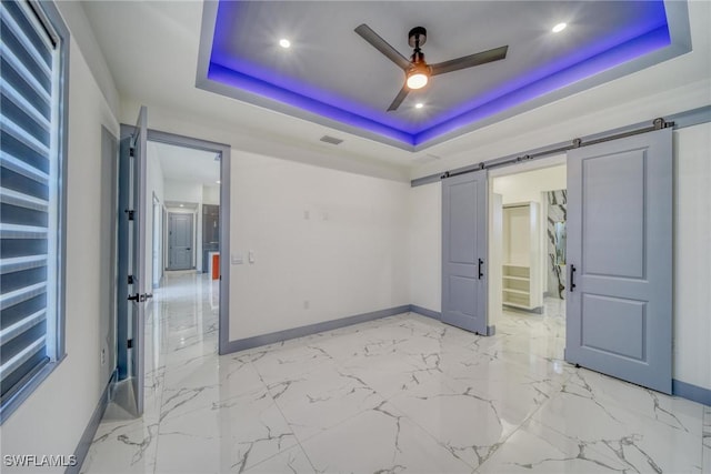 spare room featuring a barn door, visible vents, a tray ceiling, and baseboards