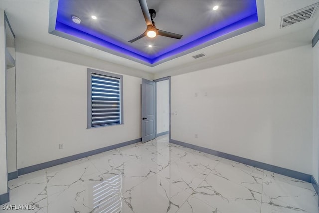 empty room featuring a tray ceiling, a ceiling fan, visible vents, and baseboards