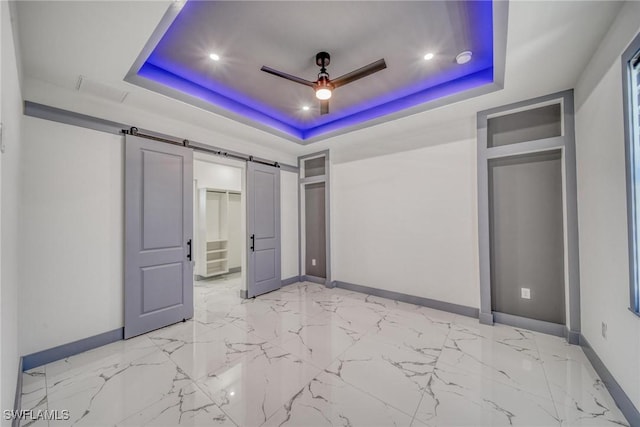 unfurnished bedroom with marble finish floor, a tray ceiling, a barn door, and baseboards