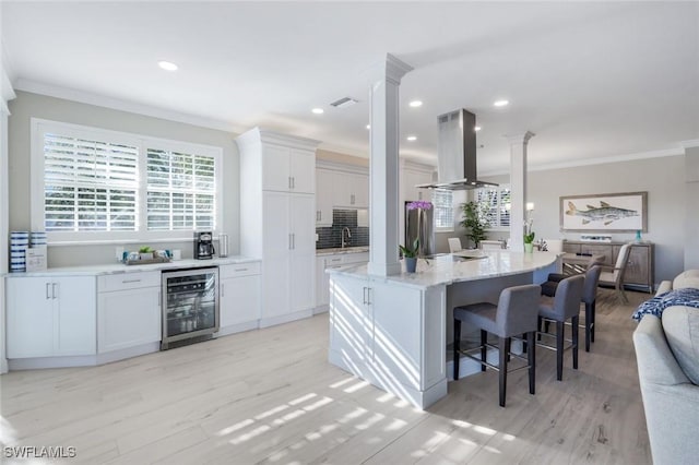 kitchen featuring decorative columns, beverage cooler, visible vents, freestanding refrigerator, and island exhaust hood