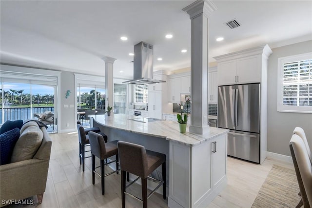 kitchen featuring decorative columns, visible vents, freestanding refrigerator, open floor plan, and island range hood