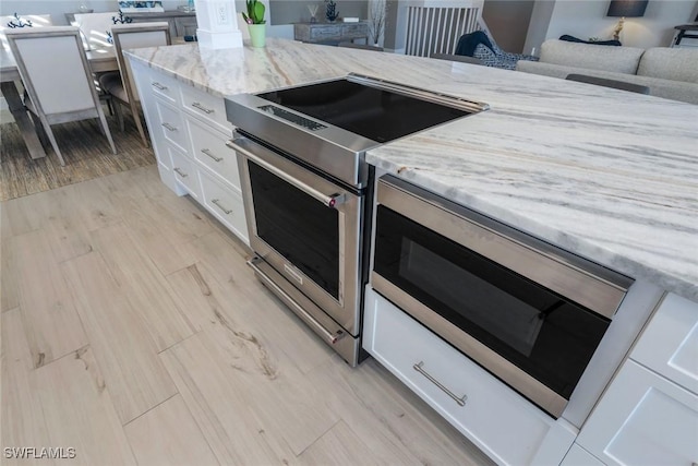 kitchen with light stone counters, light wood-style flooring, white cabinetry, open floor plan, and stainless steel range