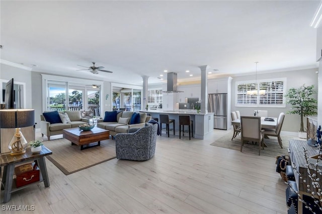 living room featuring light wood-style flooring, ornamental molding, ceiling fan with notable chandelier, ornate columns, and recessed lighting