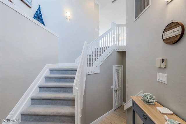 stairs featuring wood finished floors, a towering ceiling, and baseboards