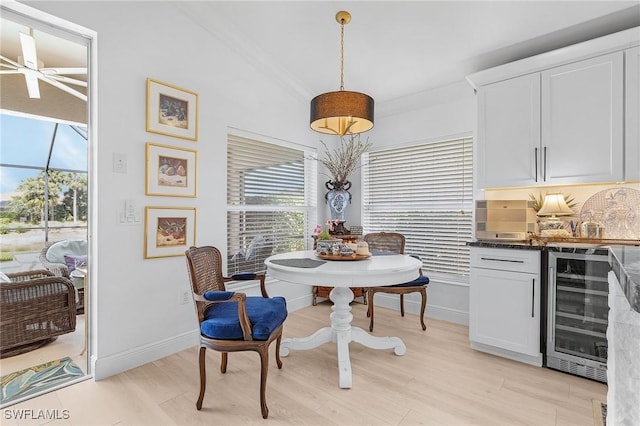 dining area featuring light wood finished floors, crown molding, baseboards, wine cooler, and a bar