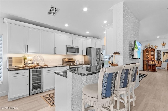 kitchen with beverage cooler, stainless steel appliances, a kitchen bar, and light wood-style floors