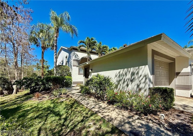 view of side of property with a lawn, an attached garage, and stucco siding