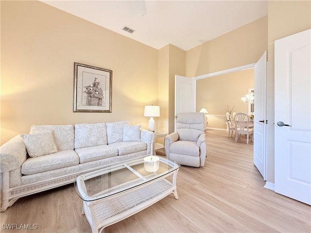 living area featuring light wood finished floors, baseboards, visible vents, and a notable chandelier