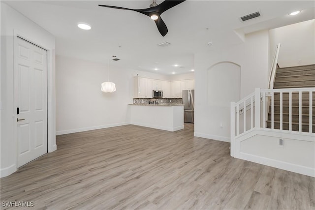 unfurnished living room with visible vents, ceiling fan, baseboards, stairway, and light wood-style floors