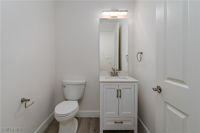 bathroom featuring baseboards, toilet, wood finished floors, and vanity