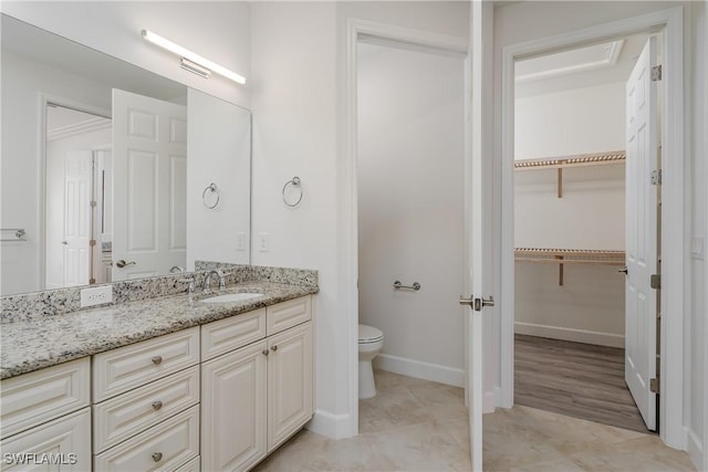 bathroom with baseboards, toilet, a spacious closet, and vanity