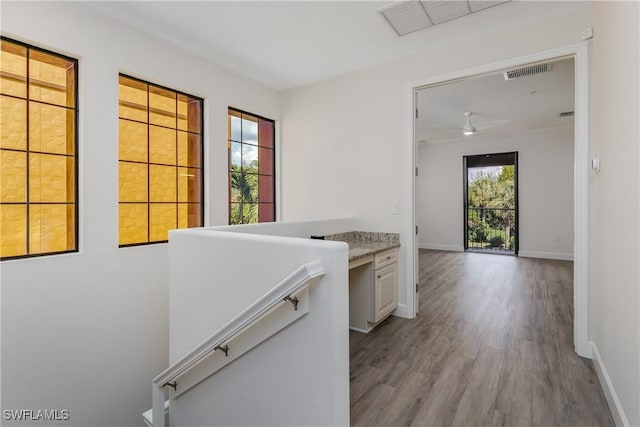 hall with an upstairs landing, wood finished floors, visible vents, and baseboards