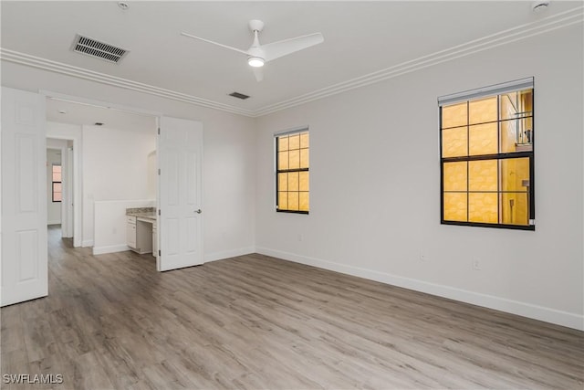 empty room with wood finished floors, baseboards, visible vents, ceiling fan, and ornamental molding