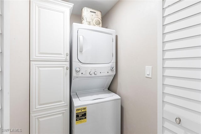 clothes washing area featuring stacked washer and dryer and cabinet space