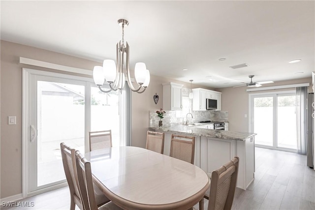 dining room featuring ceiling fan with notable chandelier, baseboards, visible vents, and light wood-style floors