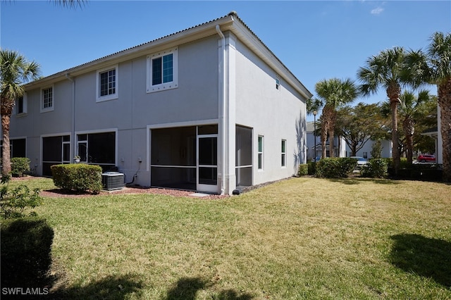 rear view of property featuring a sunroom, central air condition unit, a lawn, and stucco siding