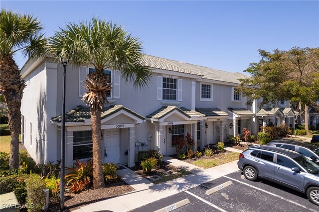 view of property featuring a tiled roof, stucco siding, and uncovered parking