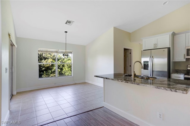 kitchen with a sink, dark stone counters, stainless steel fridge with ice dispenser, white microwave, and vaulted ceiling