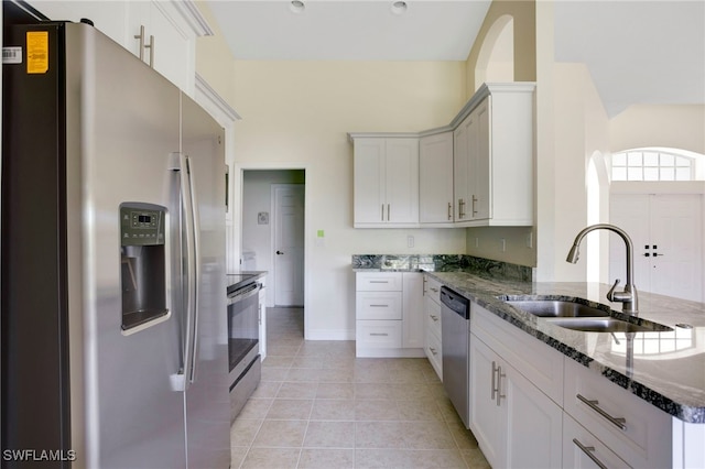 kitchen featuring a sink, dark stone countertops, stainless steel appliances, a peninsula, and light tile patterned floors