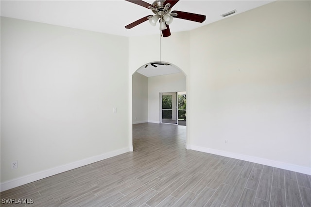 unfurnished room featuring arched walkways, visible vents, light wood finished floors, and baseboards