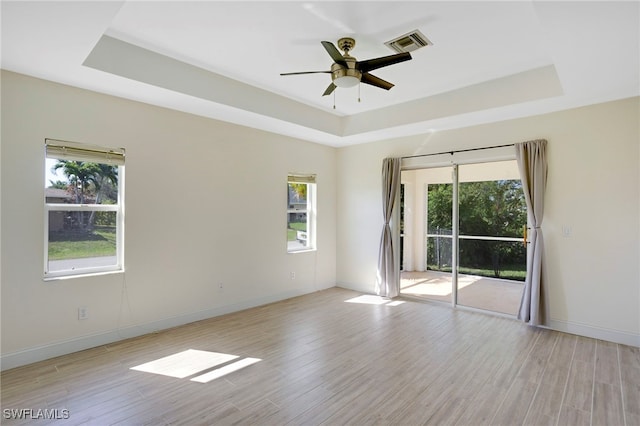 spare room featuring a tray ceiling, a healthy amount of sunlight, visible vents, and light wood-type flooring