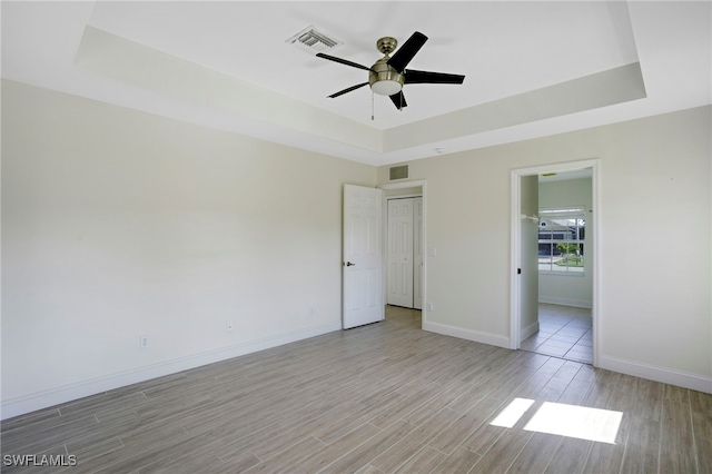 unfurnished bedroom with a tray ceiling, visible vents, and light wood finished floors