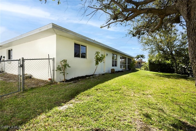 view of property exterior featuring a gate, stucco siding, a yard, and fence