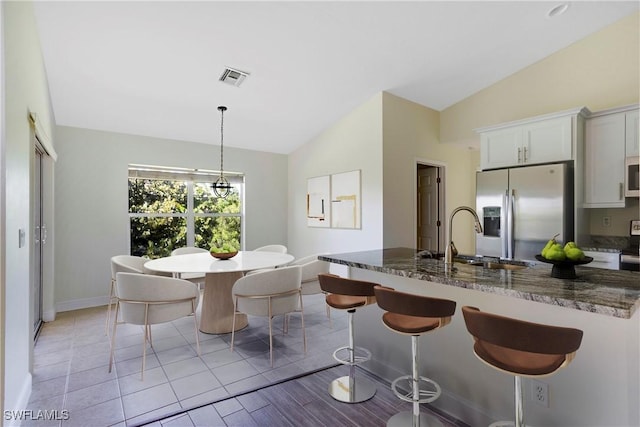 kitchen with visible vents, a breakfast bar, a sink, stainless steel fridge with ice dispenser, and lofted ceiling