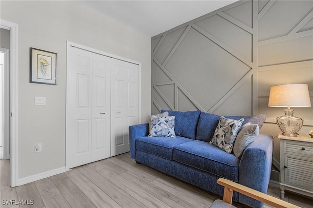 living room featuring a decorative wall, baseboards, and light wood finished floors