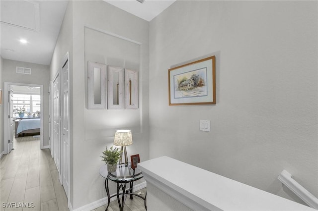 hall with visible vents, light wood-style flooring, and baseboards