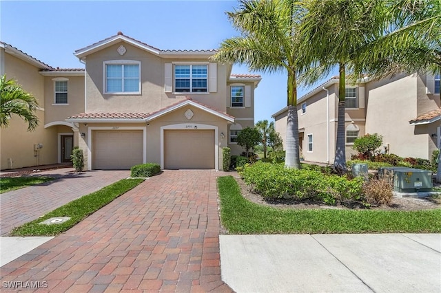 mediterranean / spanish-style house with a tiled roof, an attached garage, stucco siding, central air condition unit, and decorative driveway