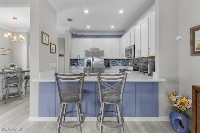 kitchen with visible vents, backsplash, white cabinetry, stainless steel appliances, and a peninsula