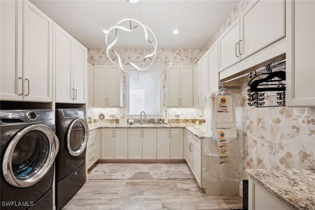 clothes washing area featuring wallpapered walls, washing machine and dryer, an inviting chandelier, cabinet space, and a sink