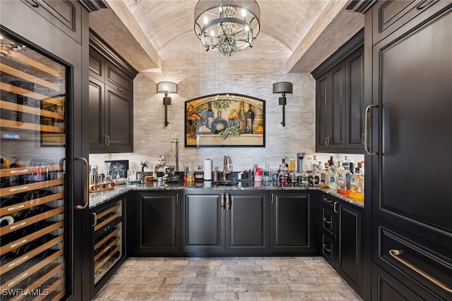 bar featuring beverage cooler, wet bar, vaulted ceiling, stone finish flooring, and a chandelier