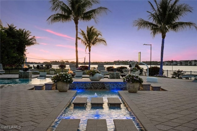 pool at dusk with a patio area, fence, and a fenced in pool