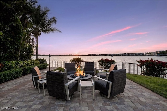 patio terrace at dusk featuring fence, a fire pit, and a water view