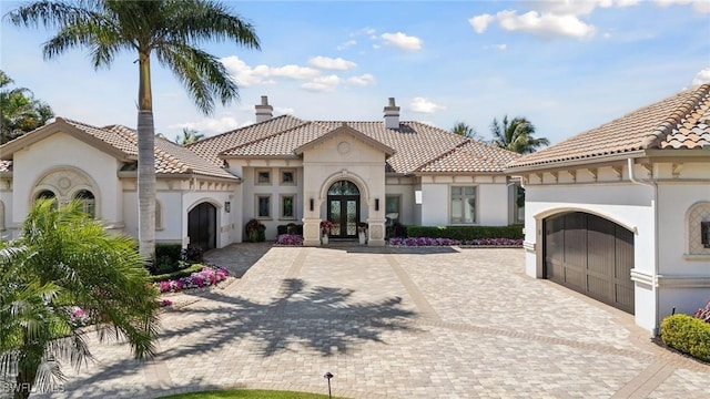 mediterranean / spanish house featuring a tile roof, stucco siding, french doors, decorative driveway, and a garage