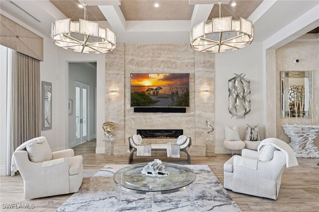 living area featuring wood finished floors, baseboards, a tray ceiling, a notable chandelier, and a large fireplace