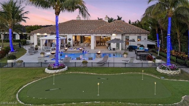 pool at dusk with a fenced in pool, fence, a yard, and a patio area