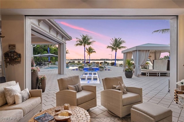 patio terrace at dusk with a gazebo, an outdoor pool, an outdoor living space, and a water view