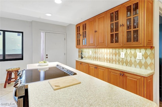 kitchen with backsplash, brown cabinets, and glass insert cabinets