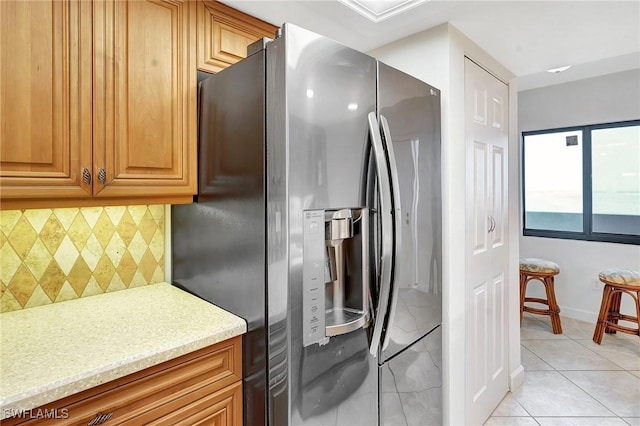 kitchen with light tile patterned floors, light stone countertops, baseboards, decorative backsplash, and stainless steel fridge