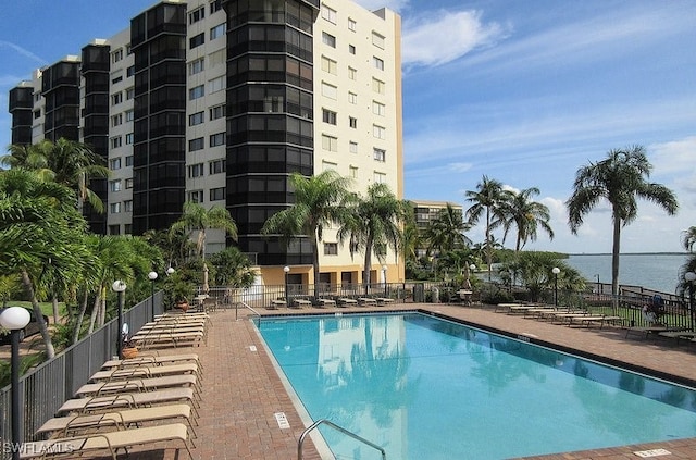 community pool featuring a patio area, a water view, and fence