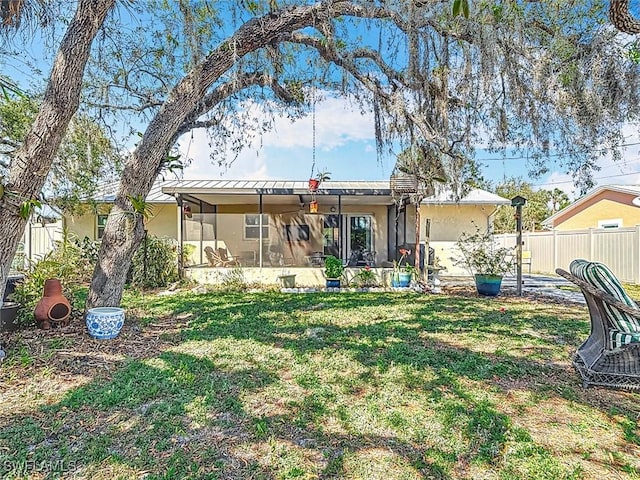 rear view of property with a yard, fence, a sunroom, and stucco siding